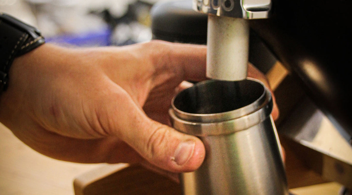 Hand greift nach einem Auffangbecher einer Kaffeemühle